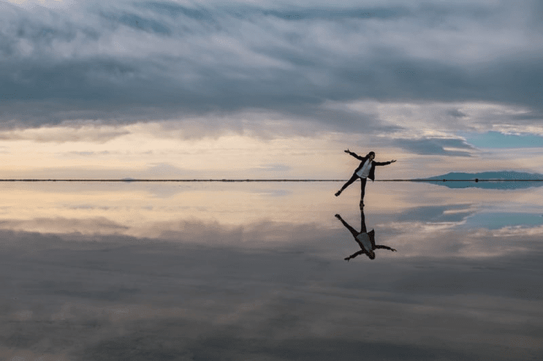 person walking over slight layer of water on sand reflecting off the sky